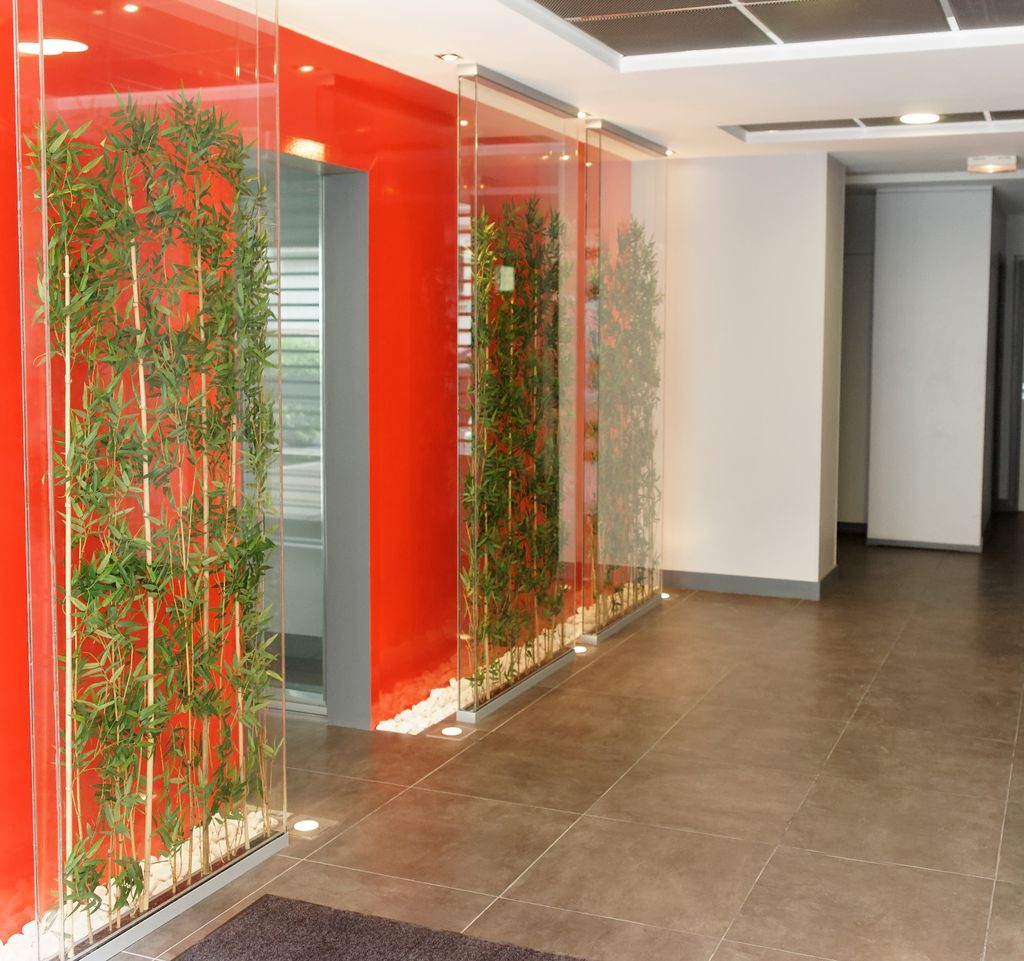 Accueil des bureaux CGE : paroi laquée rouge, bambous sous verre, sol en grès.