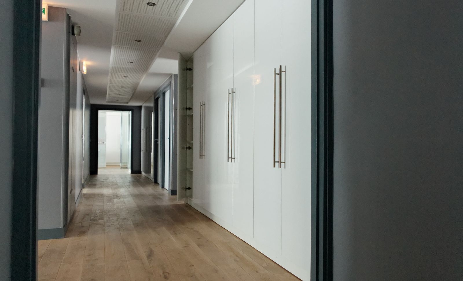 Couloir des bureaux CGE bordé de rangements blancs toute hauteur, parquet en chêne.