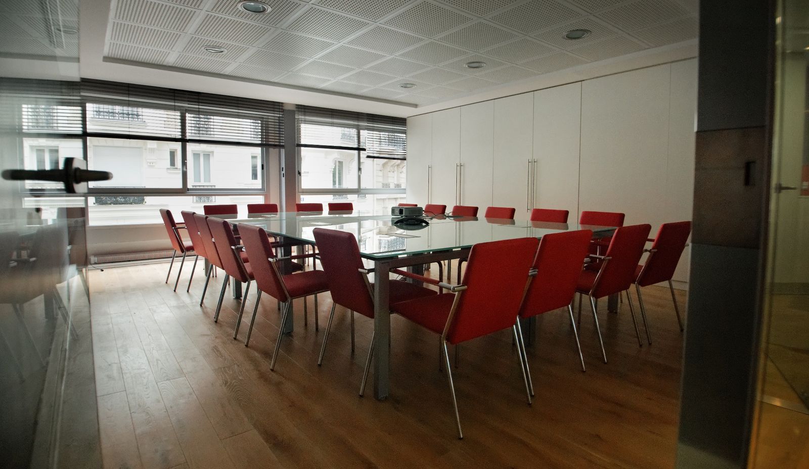 Salle de réunion des bureaux CGE : grande table en verre, sièges rouges, fenêtres sur des façades parisiennes.