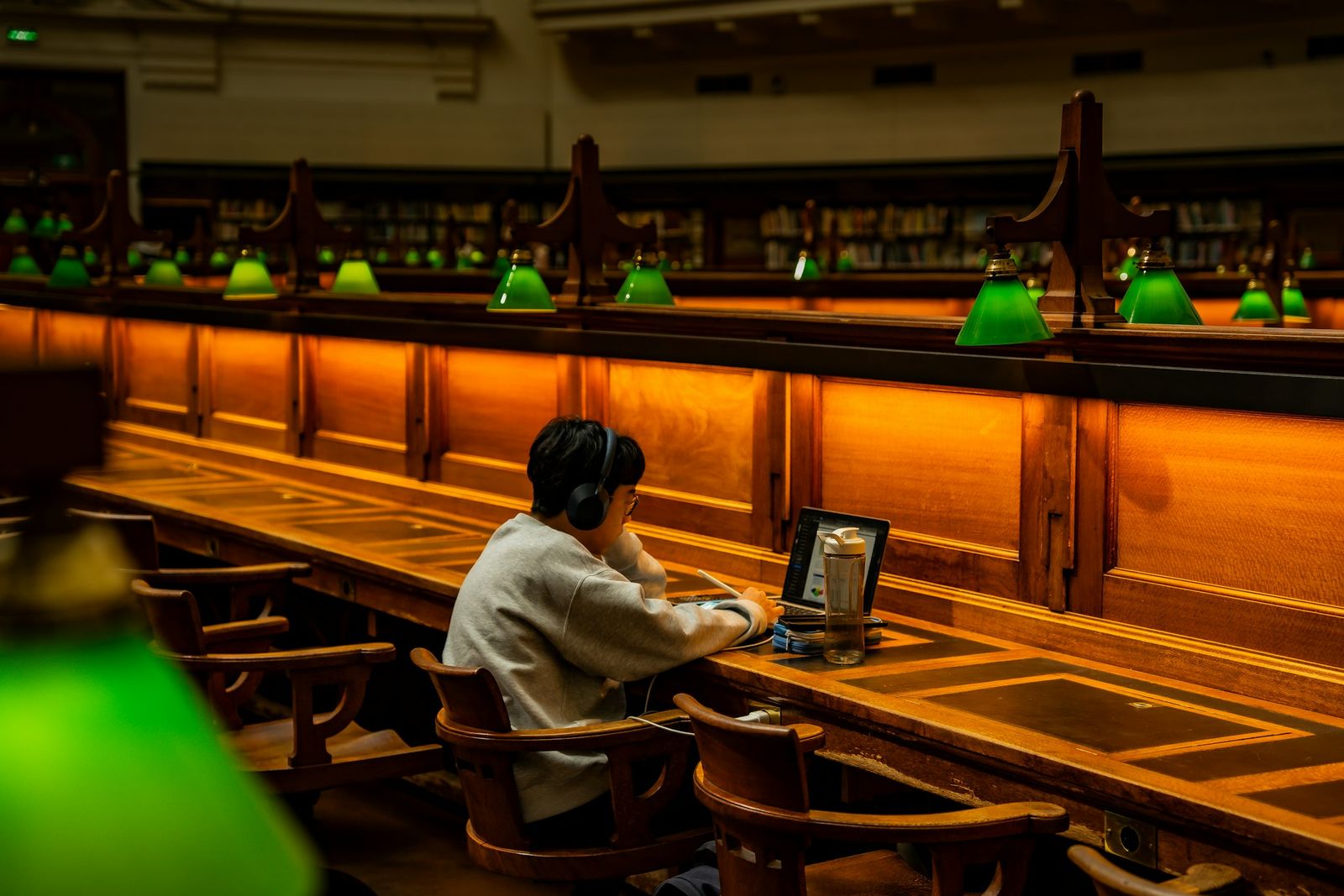 Personne concentrée à une longue table de bibliothèque éclairée par des lampes.